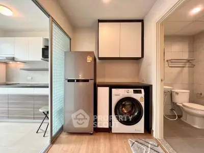 Modern apartment kitchen with washing machine and fridge, featuring sleek cabinetry and open layout.
