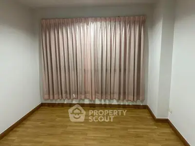 Spacious empty room with elegant wooden flooring and soft pink curtains