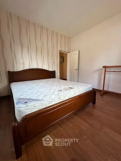Spacious bedroom with wooden flooring and stylish wallpaper, featuring a comfortable bed and ample natural light.