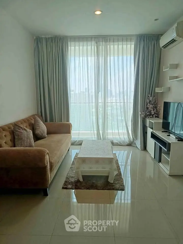 Modern living room with plush sofa, TV unit, and large window offering city views.