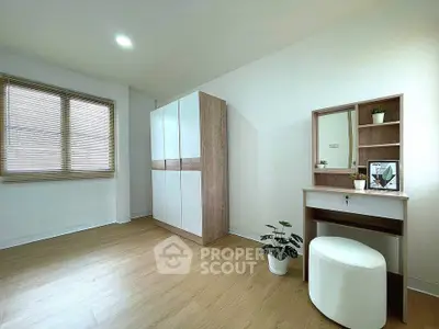 Spacious bedroom with modern wardrobe and vanity set, featuring elegant wooden flooring and natural light.