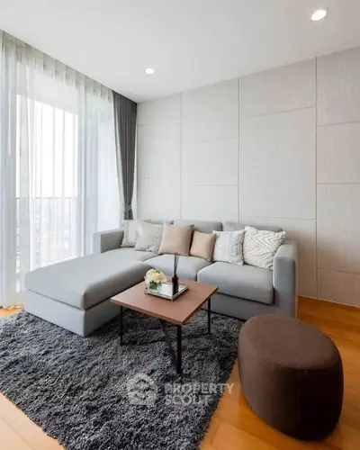 Modern living room with stylish gray sofa, cozy rug, and natural light from large windows.