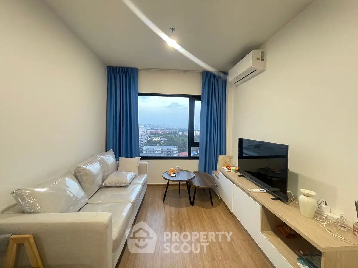 Modern living room with city view, cozy sofa, and sleek TV setup.