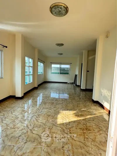 Spacious sunlit room with marble flooring and large windows, perfect for versatile living space.