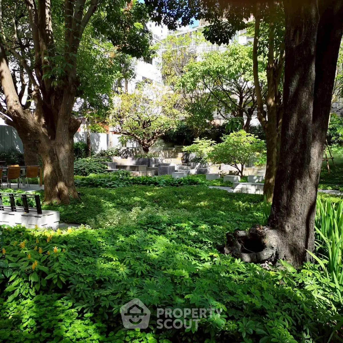 Lush green garden with mature trees and serene seating area in residential complex.