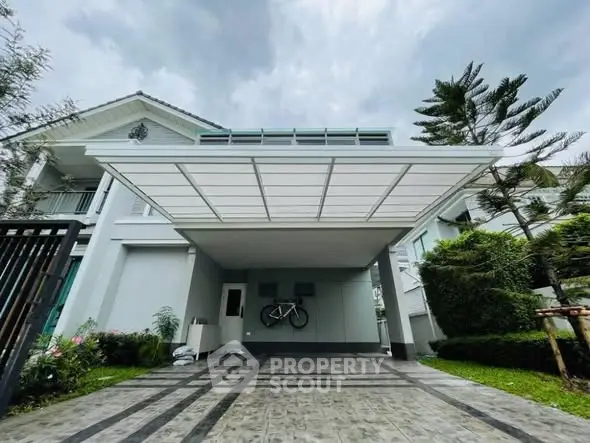 Modern house with spacious carport and lush garden under cloudy sky.