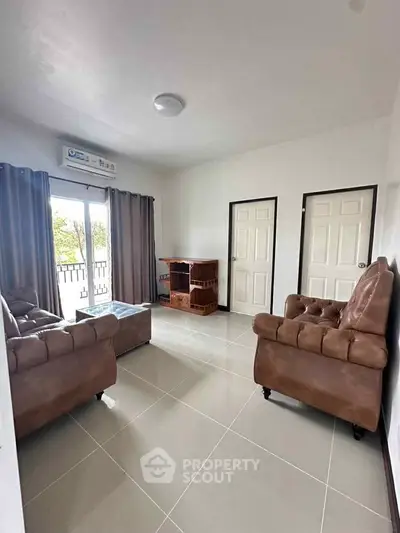 Spacious living room with elegant brown leather sofas and natural light from balcony.
