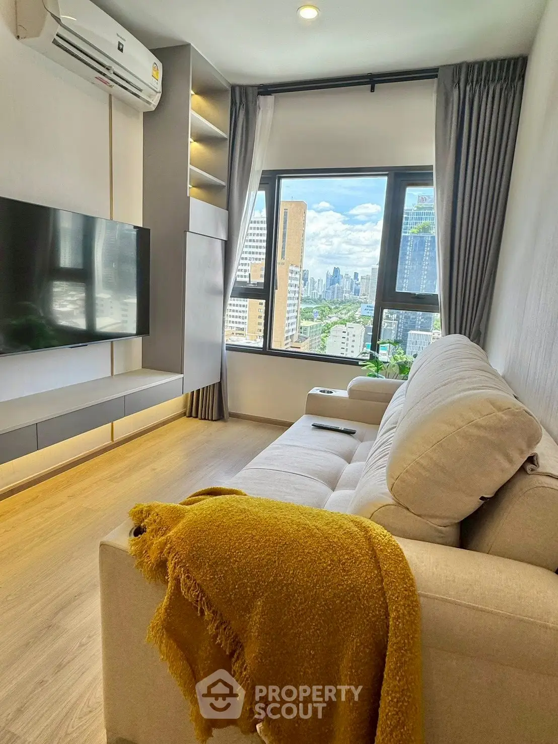 Modern living room with city view, cozy sofa, and wall-mounted TV in high-rise apartment.