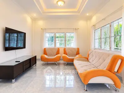 Spacious living room with modern orange sofas and large windows offering natural light.
