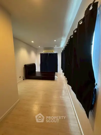Spacious bedroom with elegant black curtains and wooden flooring, perfect for modern living.