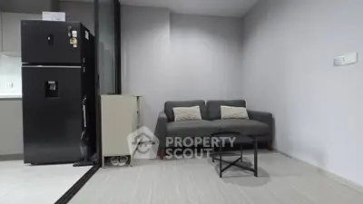 Modern living room with sleek gray sofa and compact black refrigerator in a minimalist apartment.
