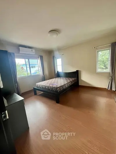 Spacious bedroom with wooden flooring and natural light from two windows.