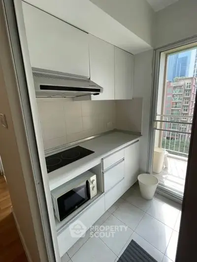 Compact modern kitchen with sleek white cabinetry and balcony access in urban apartment.