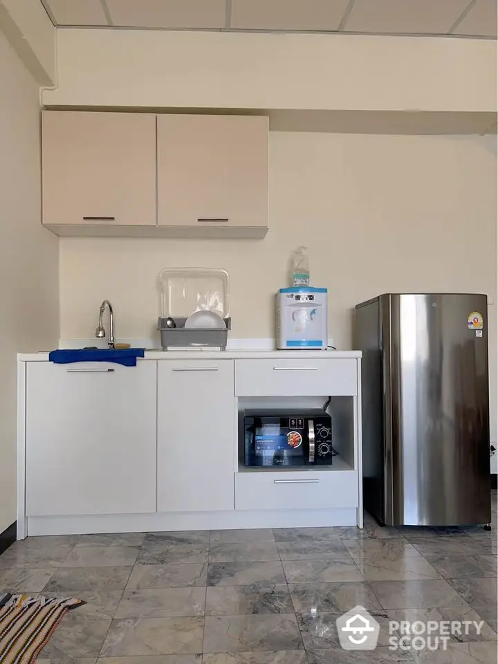 Modern kitchen with sleek cabinets, stainless steel fridge, and marble flooring.