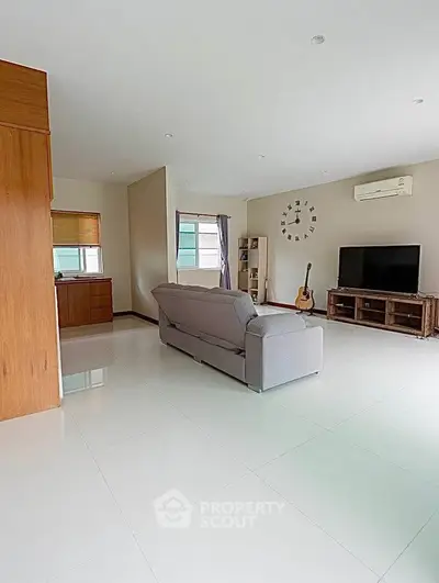 Spacious living room with modern decor, featuring a large sofa, wall-mounted TV, and natural light.