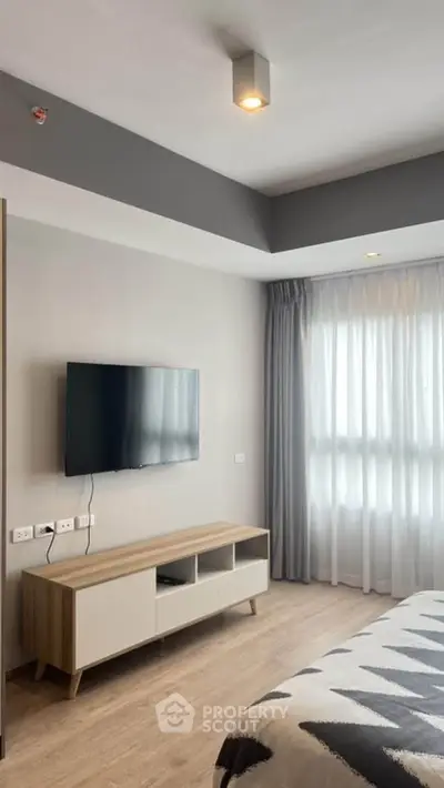 Modern bedroom with wall-mounted TV and stylish furniture in a bright apartment.