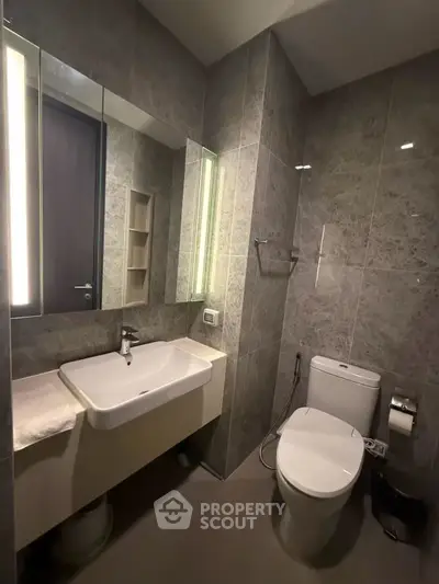 Modern bathroom with sleek fixtures and elegant gray tiles, featuring a large mirror and contemporary sink.