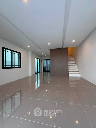 Spacious modern living room with sleek tile flooring and elegant staircase, perfect for contemporary living.