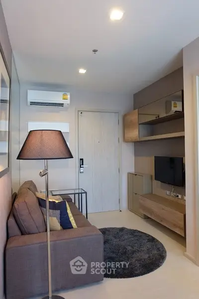 Modern living room with cozy sofa, stylish lamp, and wall-mounted TV in a compact apartment.
