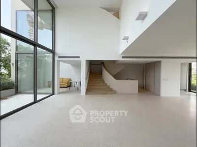 Spacious modern living room with large windows and staircase, perfect for natural light lovers.