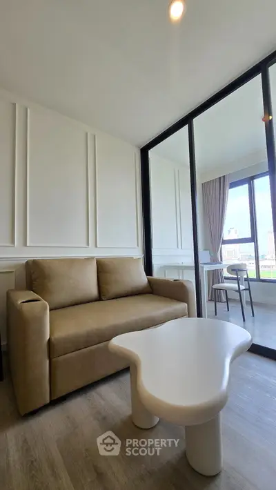 Modern living room with stylish beige sofa and unique white coffee table, featuring large windows with city view.