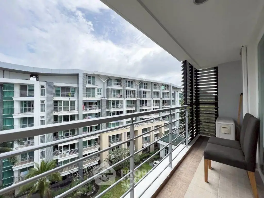 Spacious balcony with seating offering a view of modern residential buildings and lush greenery.