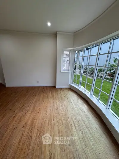 Spacious living room with large windows and garden view, featuring elegant wooden flooring.