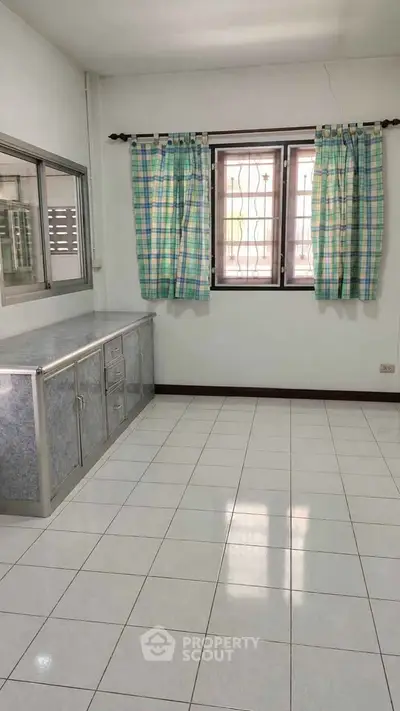 Spacious kitchen with tiled floor and large window, featuring ample storage cabinets and natural light.