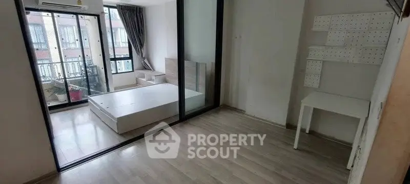 Modern apartment with glass partition and wooden flooring, featuring a compact bedroom and study area.