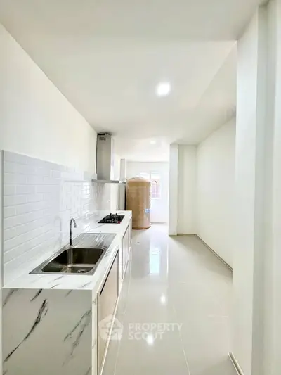 Sleek modern kitchen with white cabinetry and gas stove in a bright, narrow layout.