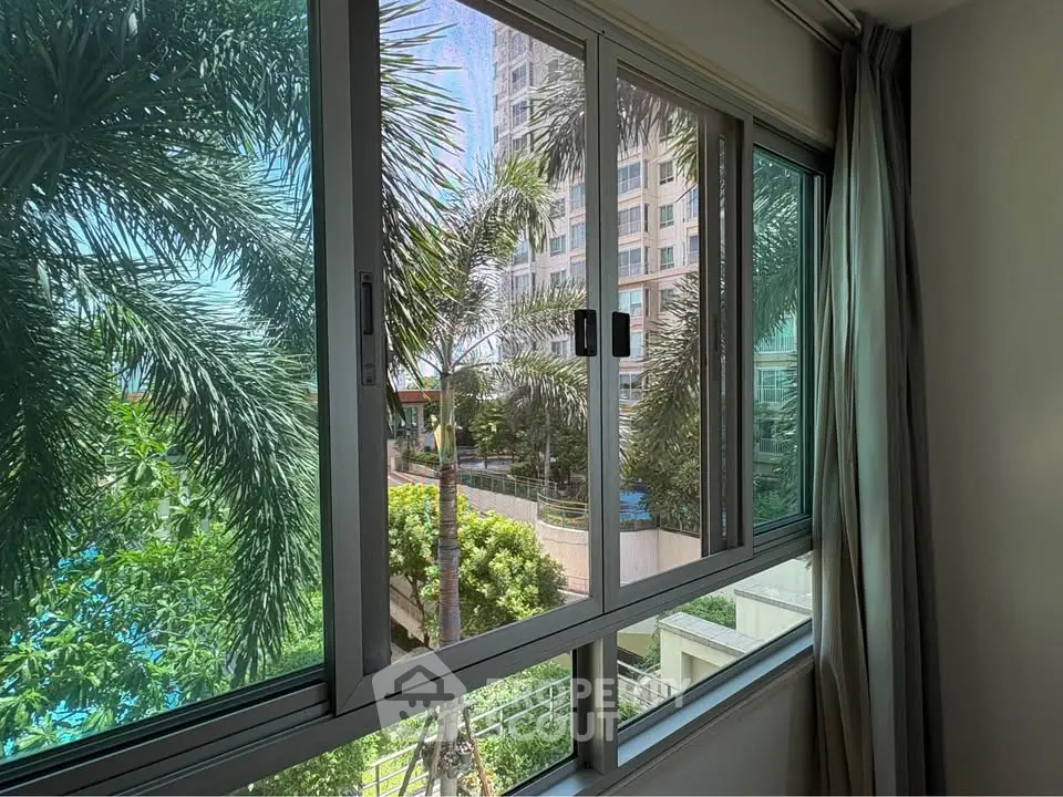 Stunning view from a modern apartment window overlooking lush greenery and a luxurious pool area.