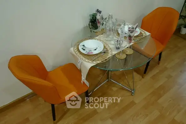 Stylish dining area with glass table and vibrant orange chairs on wooden flooring.