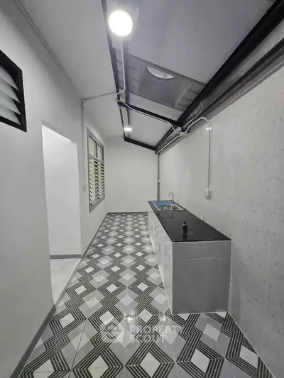 Modern kitchen with sleek design and geometric floor tiles, featuring a stainless steel sink and ample natural light.