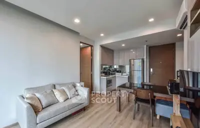 Modern open-plan living room with kitchen, featuring sleek furniture and wooden flooring.