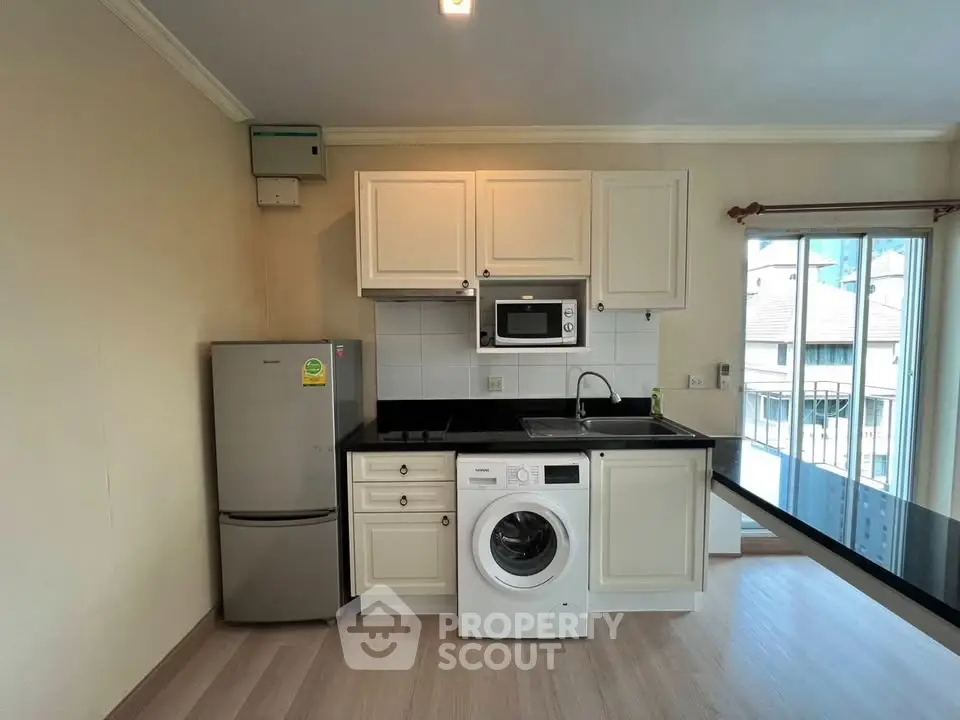 Modern kitchen with washing machine, fridge, and microwave in a bright apartment.