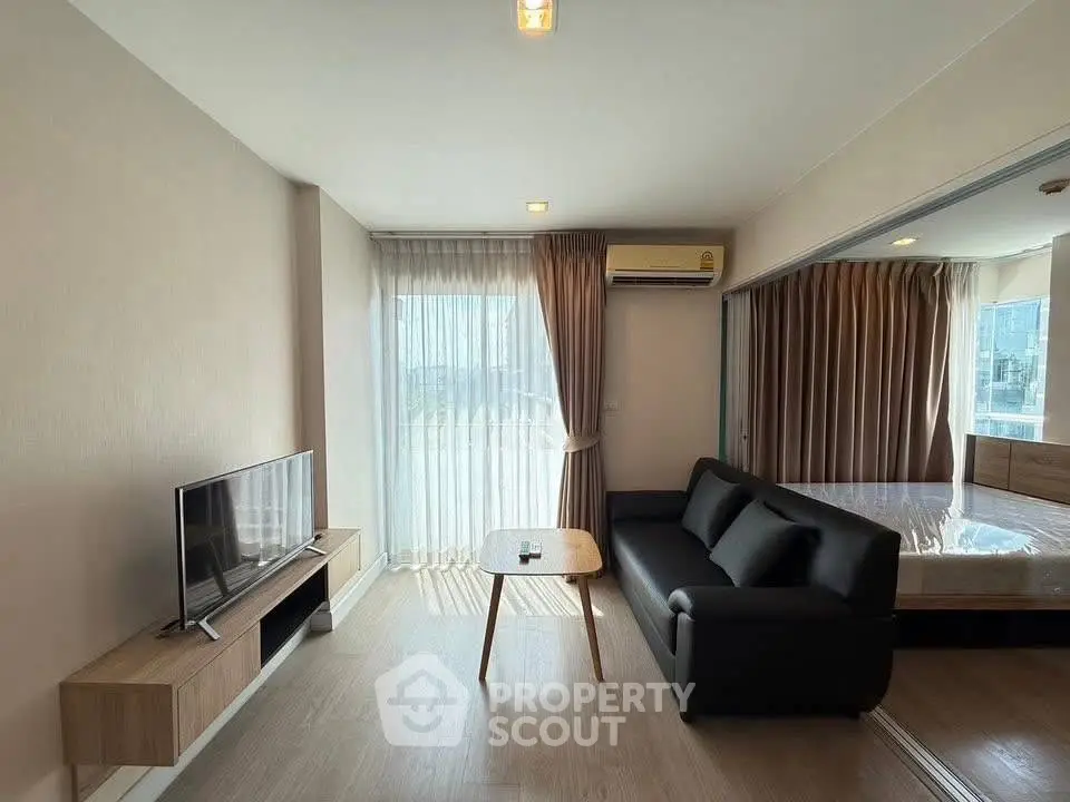 Modern living room with sleek black sofa and wall-mounted TV, adjacent to a cozy bedroom.