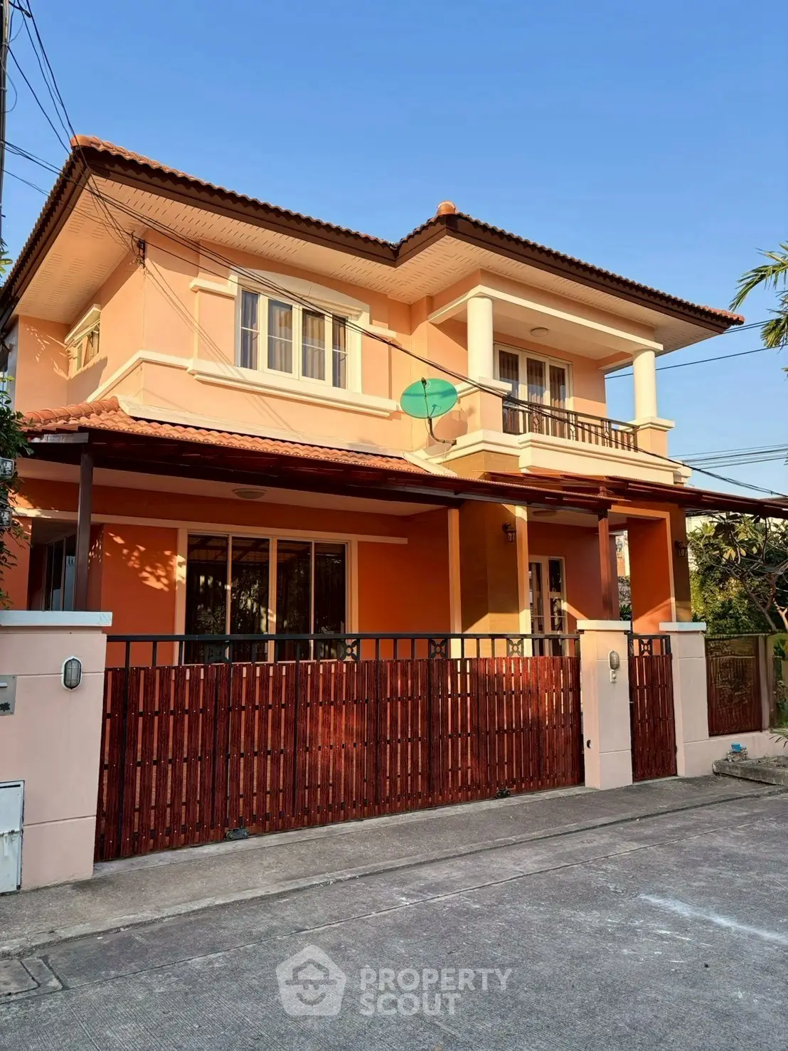 Charming two-story house with balcony and gated entrance in a serene neighborhood.