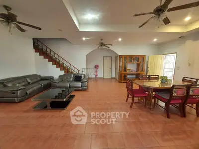 Spacious living room with terracotta tiled flooring, large leather sofas, wooden dining set, and an elegant staircase leading to the upper level.