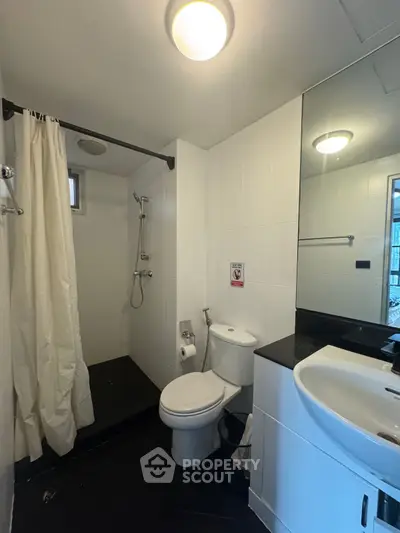 Modern bathroom with shower, toilet, and sink in sleek white and black design.