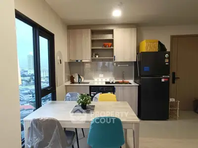 Modern kitchen with dining area and city view, featuring sleek cabinetry and colorful chairs.