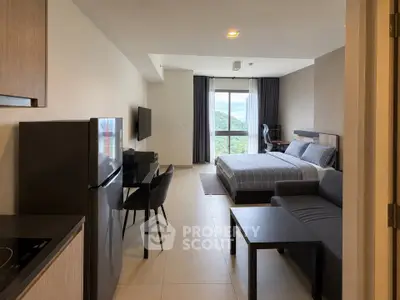 Modern studio apartment with open layout, featuring a cozy bed, sleek kitchen, and scenic window view.