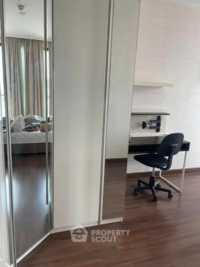 Modern bedroom with mirrored wardrobe and study desk, featuring sleek wooden flooring and natural light.
