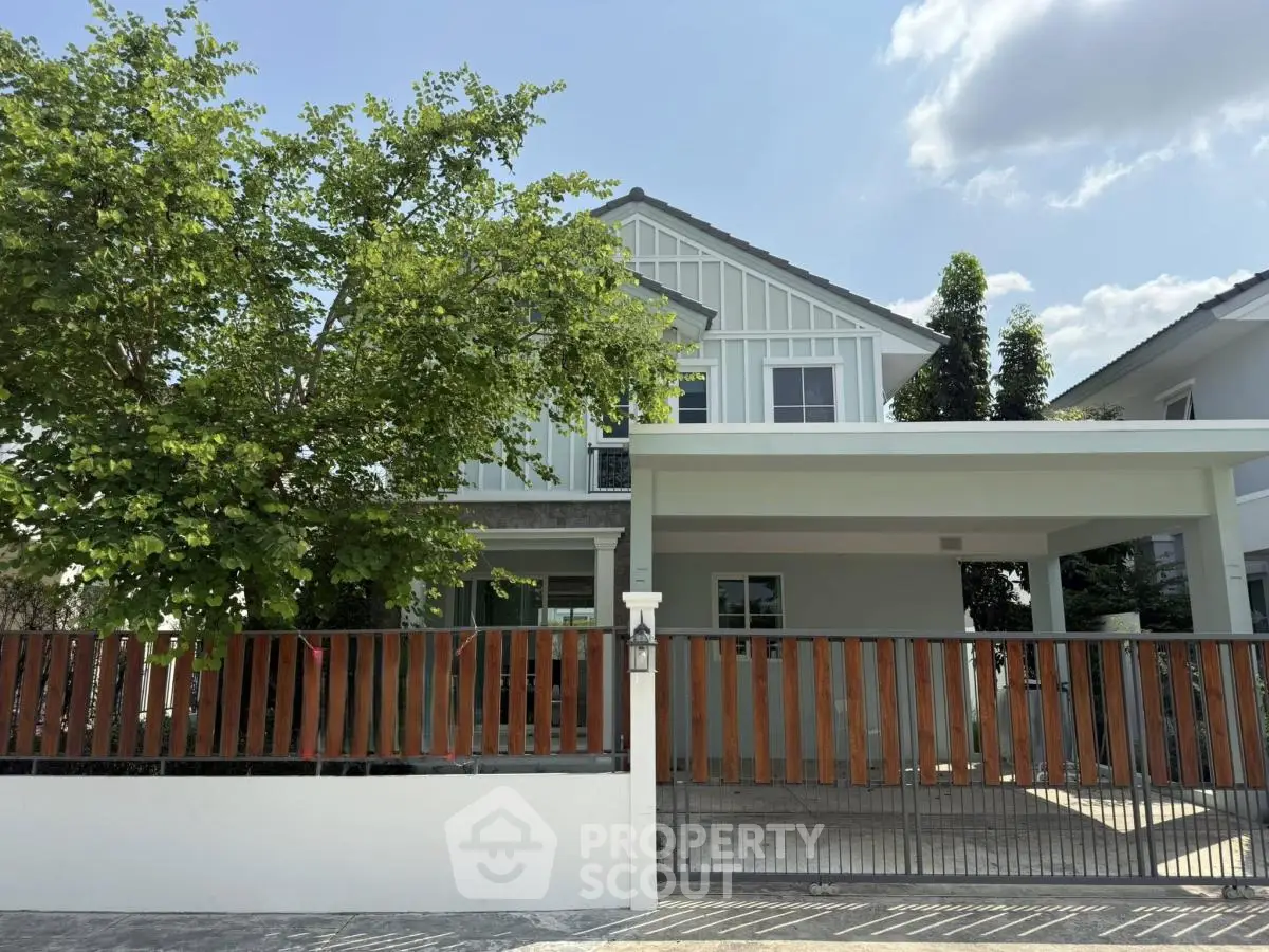 Charming two-story house with modern design and spacious driveway, surrounded by lush greenery and a stylish fence.