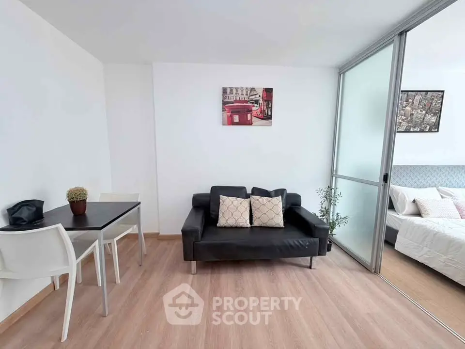 Modern living room with sleek black sofa and dining area, adjacent to a cozy bedroom with stylish decor.