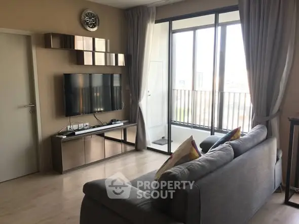 Modern living room with sleek furniture and large windows leading to a balcony.