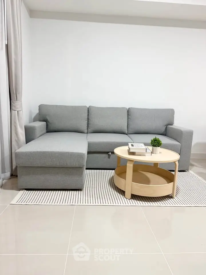 Modern living room with sleek grey sofa and stylish round coffee table on a chic striped rug.