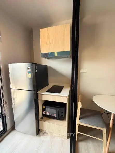 Modern compact kitchen with stainless steel fridge and dining area in cozy apartment.
