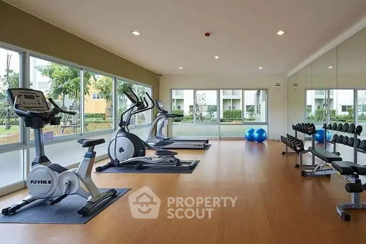 Spacious gym with modern equipment and large windows offering garden views.
