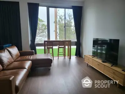 Spacious living room with large windows offering natural light and a serene view, complemented by a comfortable leather sofa and modern entertainment unit.