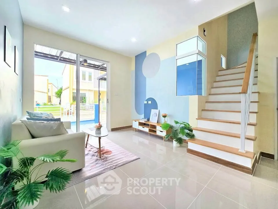 Modern living room with stylish decor and staircase, featuring large windows and natural light.